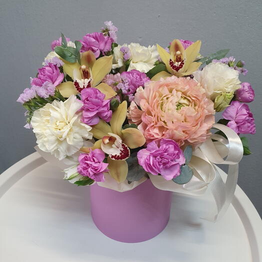 Композиция из розового ранункулюса, орхидей, фиолетового диантуса в шляпной коробке